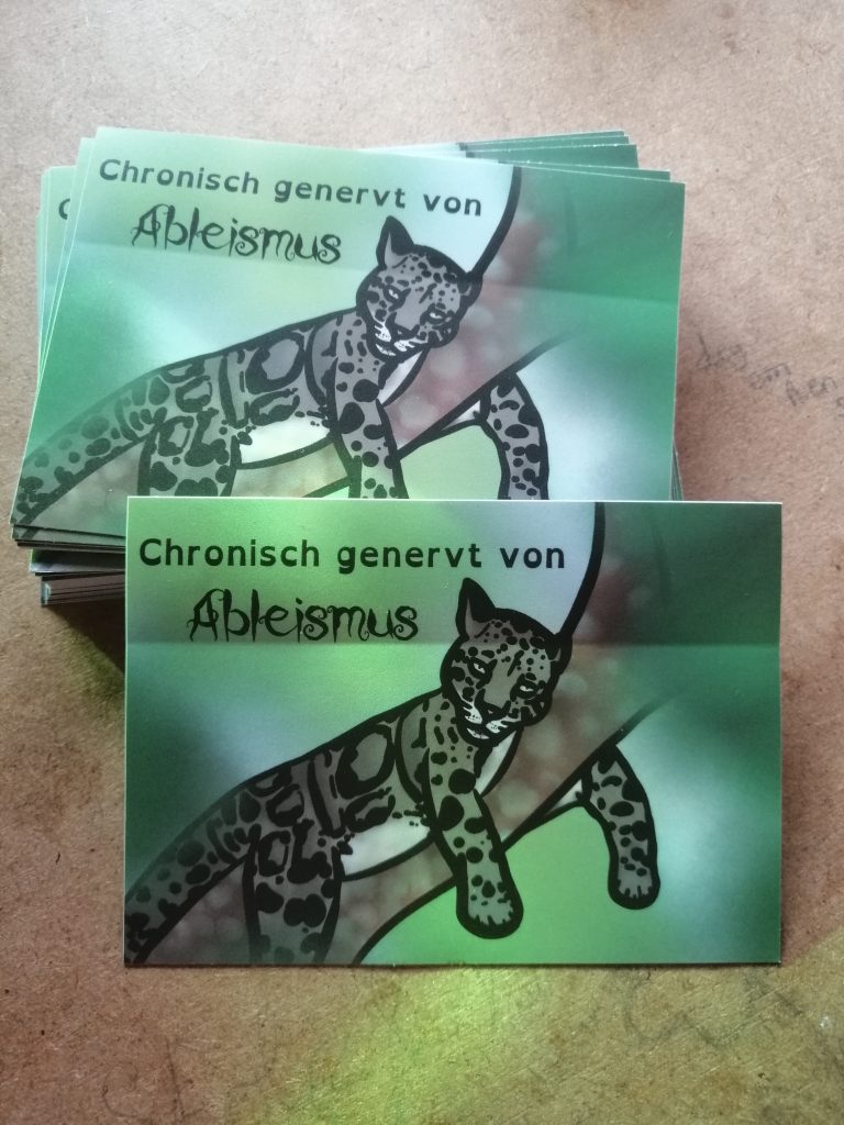 Ein Nebelparder liegt auf einem Ast. Das ist eine Wildkatze. Sie guckt genervt. Text: Chronisch genervt von Ableismus. Der Hintergrund ist grün.