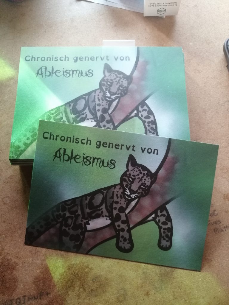 Ein Nebelparder liegt auf einem Ast. Das ist eine Wildkatze. Sie guckt genervt. Text: Chronisch genervt von Ableismus. Der Hintergrund ist grün.