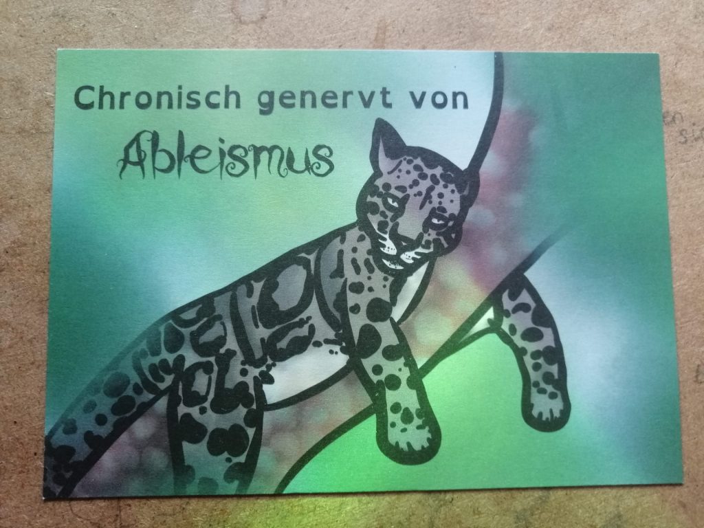 Ein Nebelparder liegt auf einem Ast. Das ist eine Wildkatze. Sie guckt genervt. Text: Chronisch genervt von Ableismus. Der Hintergrund ist grün.