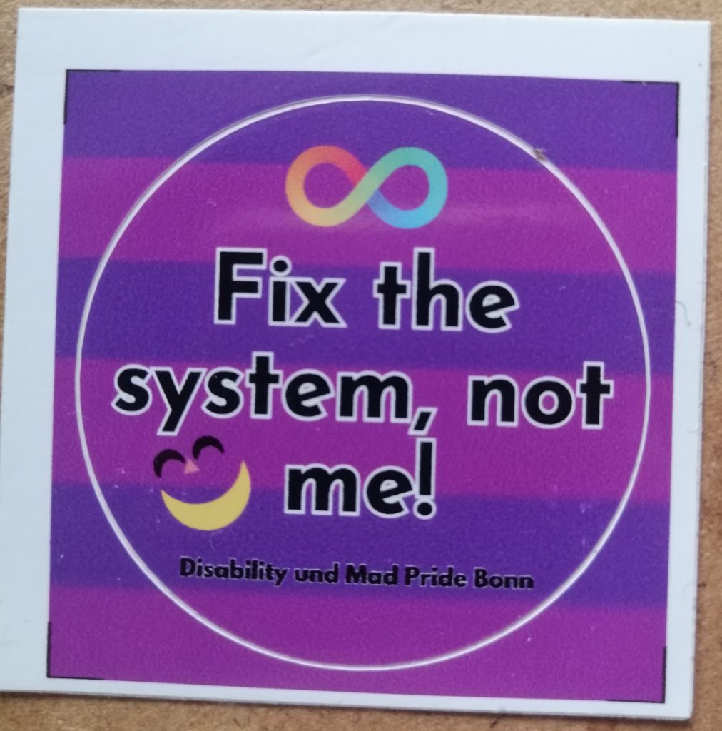 Fix the system, not me! Disability und Mad Pride Bonn. Im Hintergrund ist die Mad Pride Fahne. Die ist abwechselnd lila und pink gestreift. Über dem Text ist die Neurodivergenz-Schleife. Neben dem Text das Mad Pride Grinsen.