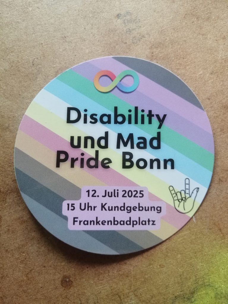 Disability und Mad Pride Bonn 12. Juli 2025 15 Uhr Kundgebung Frankenbadplatz Im Hintergrund die Disability/ CIMND* Pride Fahne: schwarz, braun, orange, rot, gelb, weiß, blau, grün, lile, pink. Der Hintergrund ist grau. Zu sehen ist die Neurodivergenz-Schleife, eine bunte liegende 8. Und die Gebärde für "I love you"