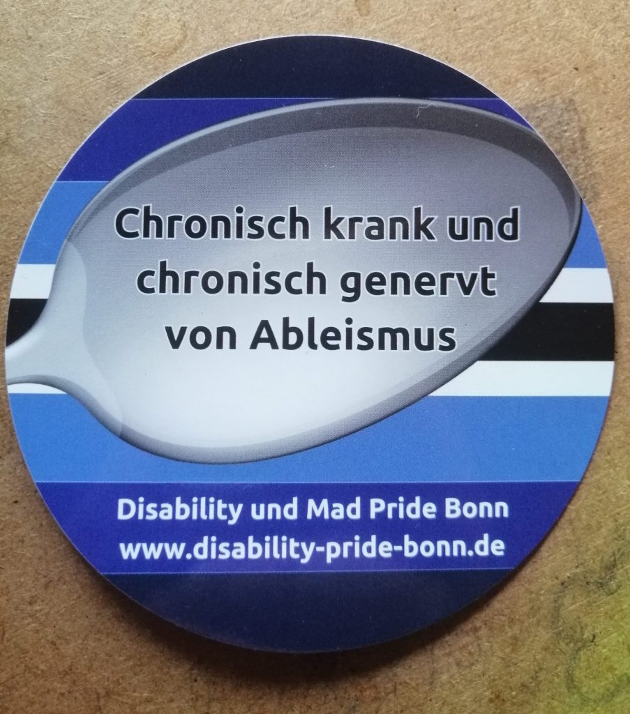 Spoonie Pride Fahne: Dunkelblau, blau, hellblau, weiß, schwarz, weiß, hellblau, blau, dunkelblau Davor zu sehen ist ein Löffel, auf dem steht: Chronisch krank und chronisch genervt von Ableismus
