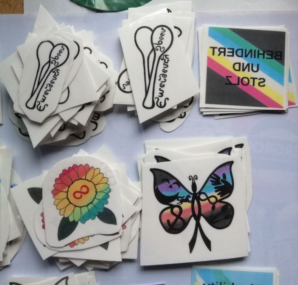 Einmal-Tattoo Motive: Autistic Pride Sonnenblume, Emergency Spoons, CIMND* Schmetterling. Und von 2024: Behindert und Stolz mit einer Pride Fahne.