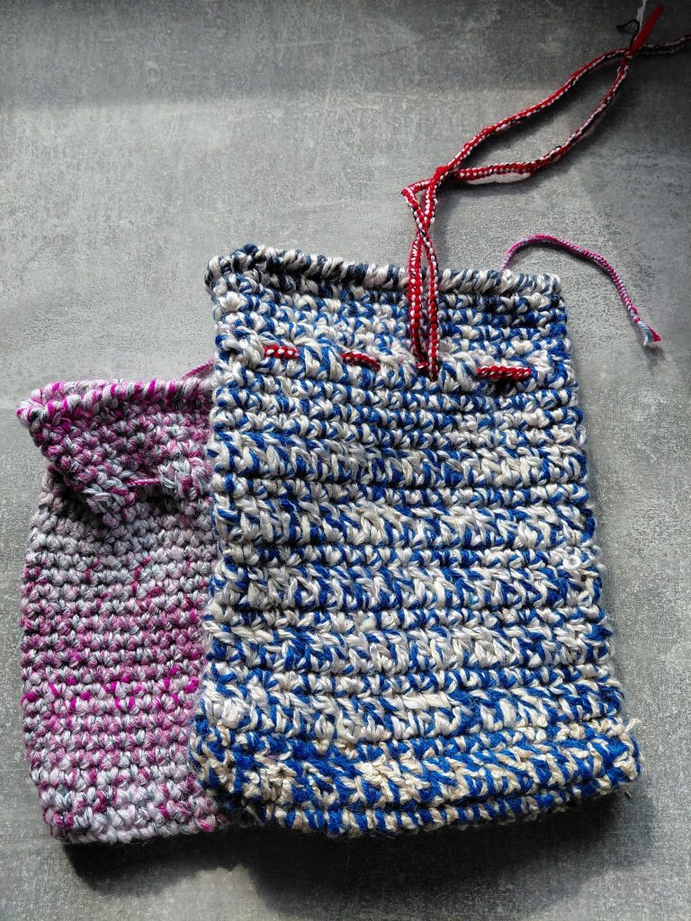 2 selbst gehäkelte Säckchen. Ein blau-weißes Sächen liegt über einem kleineren pinken.